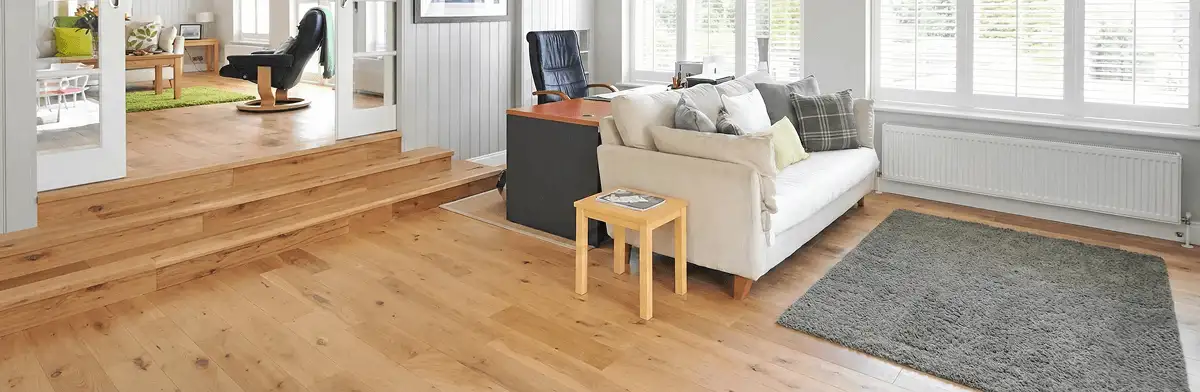 A modern living room with professionally installed laminate flooring, a beige sofa, a small side table, a gray rug, and large windows with white shutters in Columbus, GA